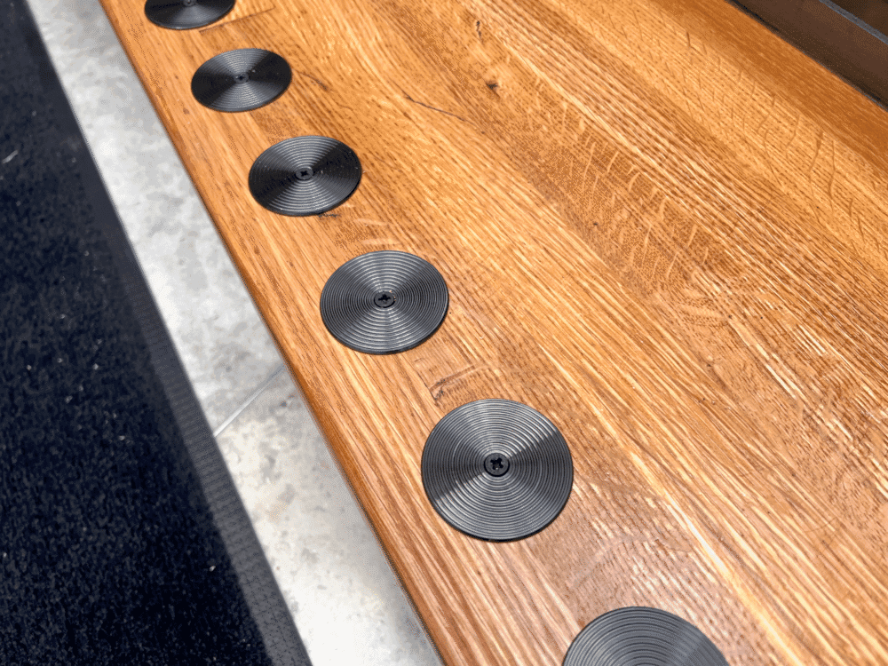 Svarta runda kontrastmarkeringar med linjerad yta på trätrappa.